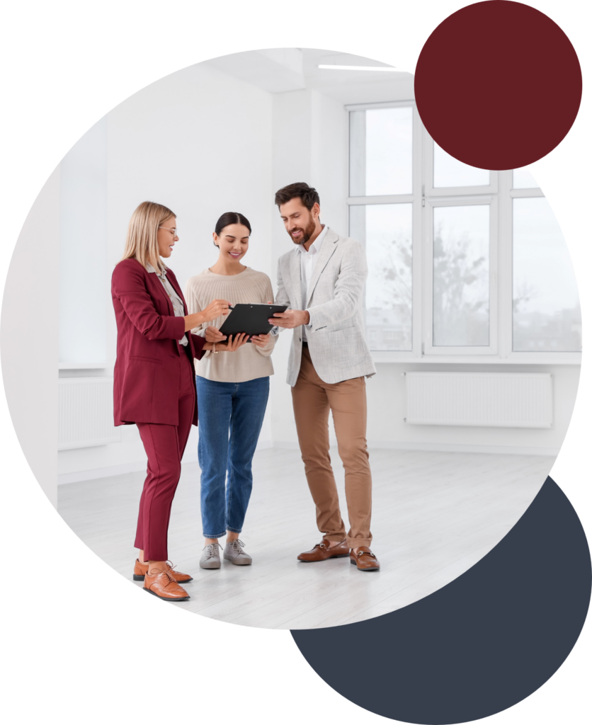 Two clients stand with a real estate agent in a vacant home looking at a tablet screen.